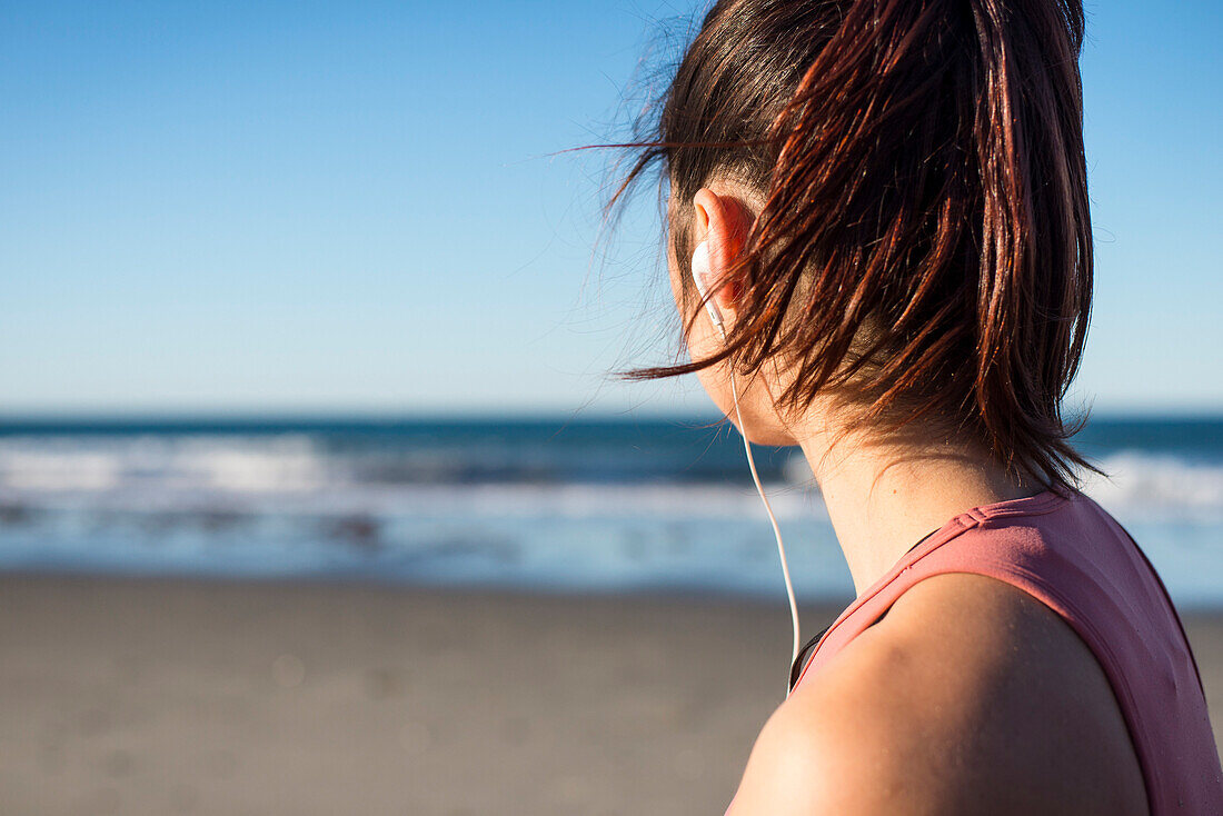 Woman in her twenties with earbuds working out during an early morning on the beach in Newport, Rhode Island