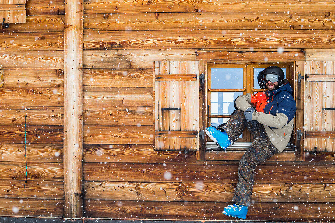 Callum Pettit sits in the window of a log cabin in full ski gear while it snows. Verbier, Switzerland