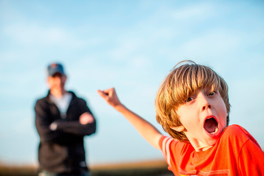 A boy yells outside, while his father stands behind him.