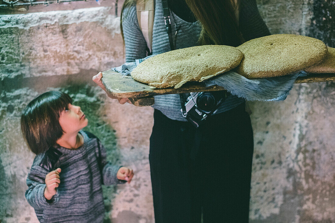Kid staring at mother while holding two Moroccan breads in hands, Medina, Marrakesh, Morocco