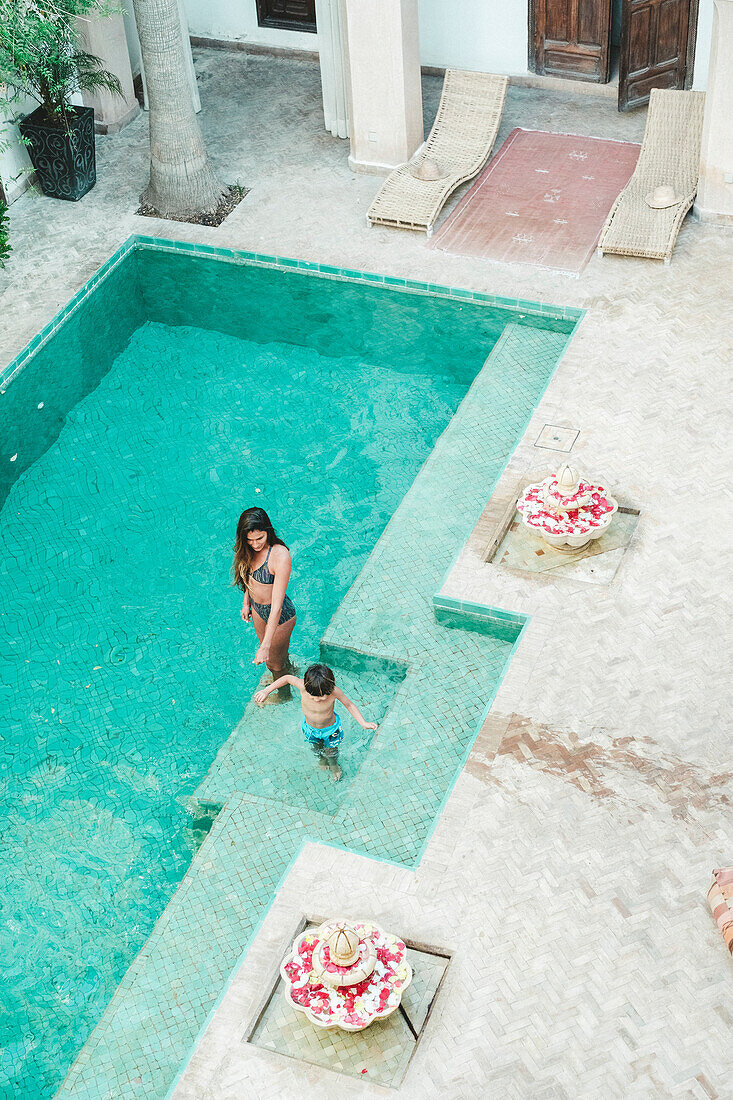 High angle view of mother in bikini with son in swimming trunks in swimming pool in Moroccan riad, Marrakech, Morocco