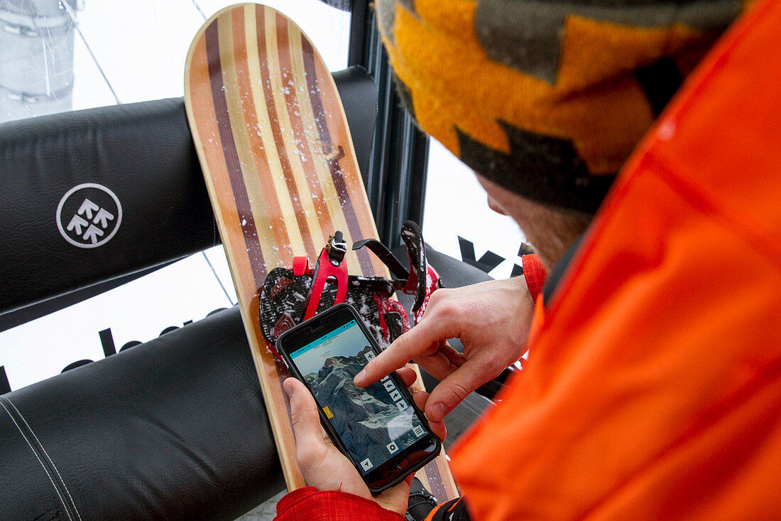 Snowboarder mit einem Telefon zur Überprüfung der freien Fahrbahn im Lift