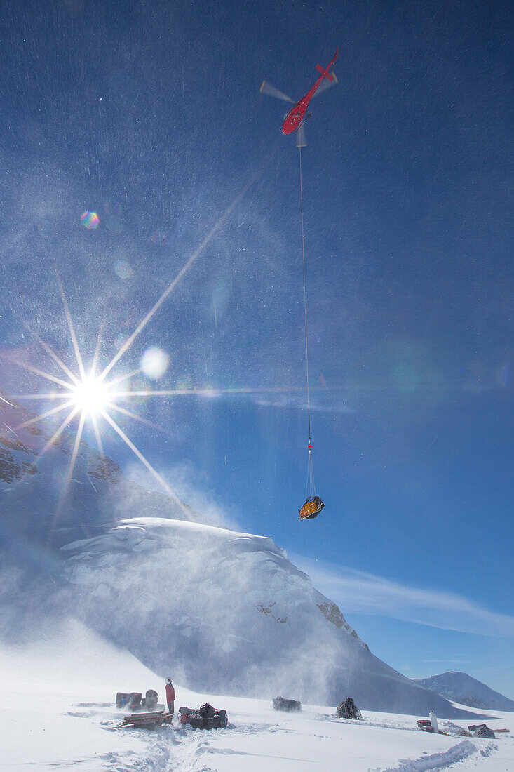 A helicopter is removing waste from a camp on Denali by sling load.