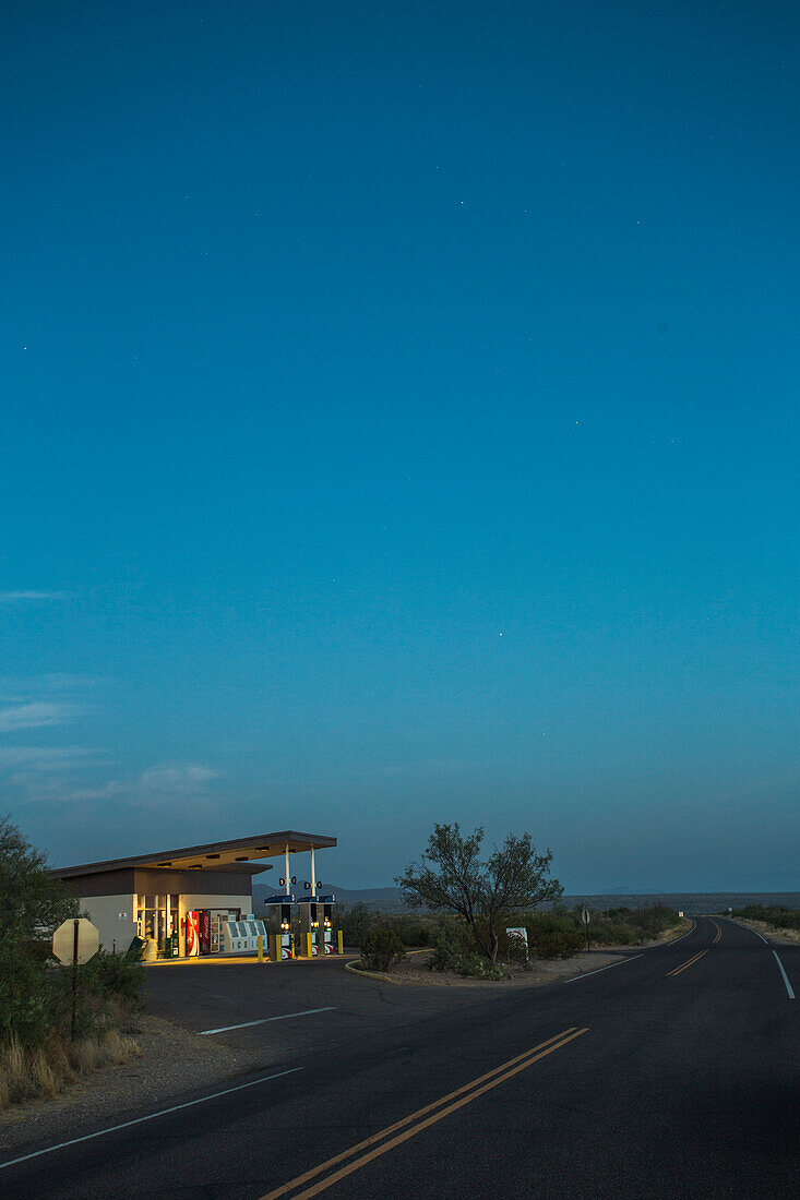 Eine Vintage Tankstelle leuchtet neben einer leeren Wüste Road in der Dämmerung