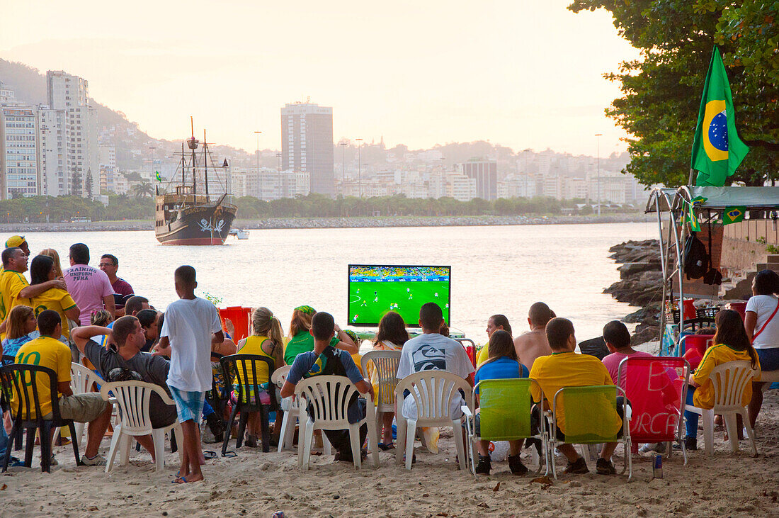 Eine Gruppe von lokalen Fußballfans beobachten ein Fußballspiel im Fernsehen am Strand