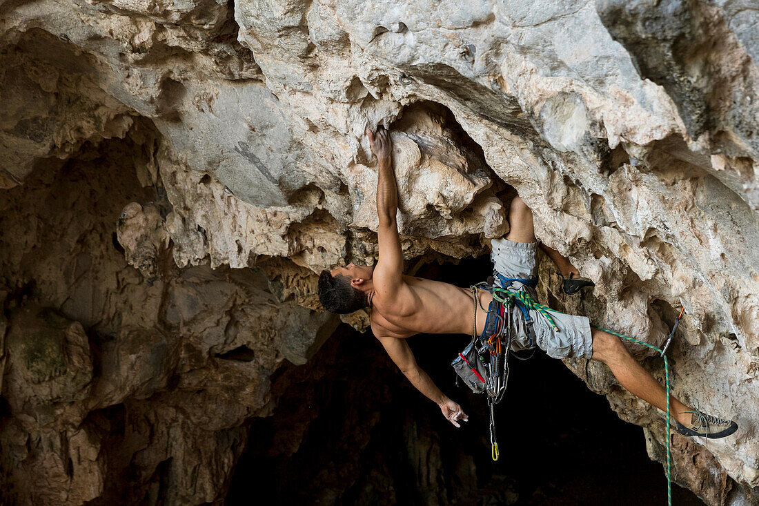 A local Cuban climber rope climbs up a cliff in Vinales, Cuba.