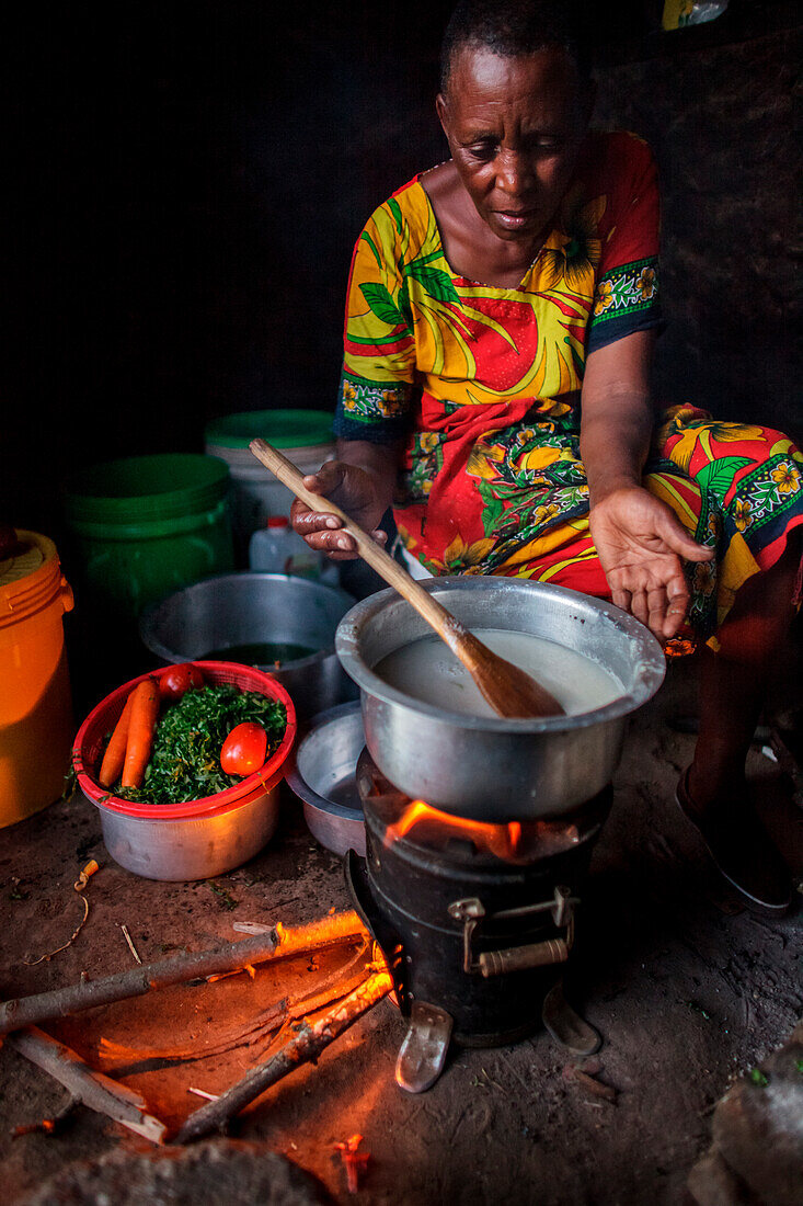 At her home near Arusha, Tanzania Solar Sister entrepreneur Julieth Mollel  prepares a dinner of ugali, vegetables and beans cooking on her clean cookstove. Ugali is a staple eaten in many countries in Africa and is cornmeal porridge. Working in her compa