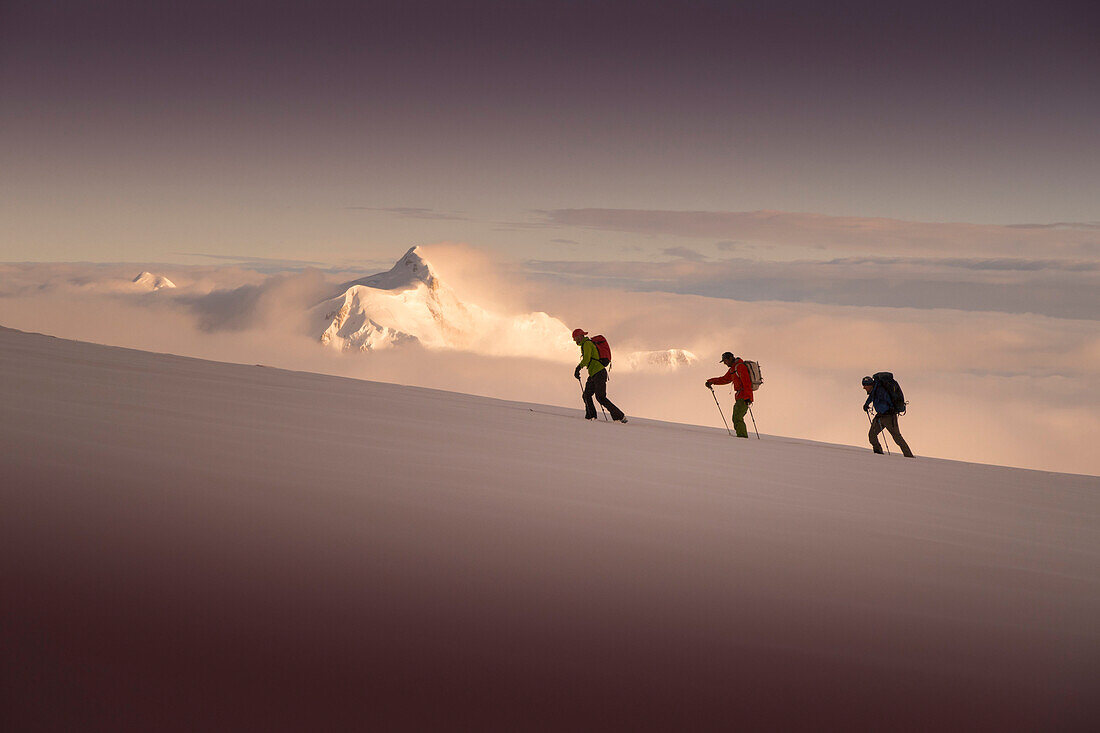 Three ski mountaineers ascending Denali, with sunset over Mount Hunter in the background. Denali National Park is a great location for backcountry skiing and mountain climbing tours.