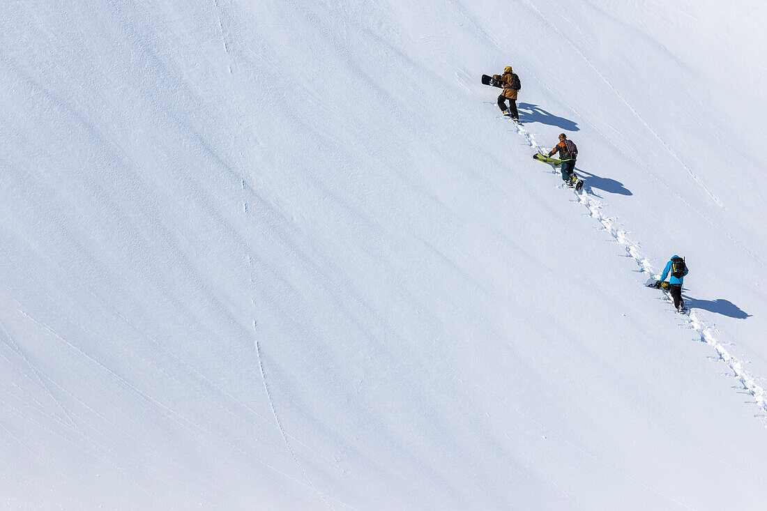 Snowboarder wandern in einer Gruppe zu einem sauberen Segeltuch des Schnees auf dem Weg zu ihren Linien