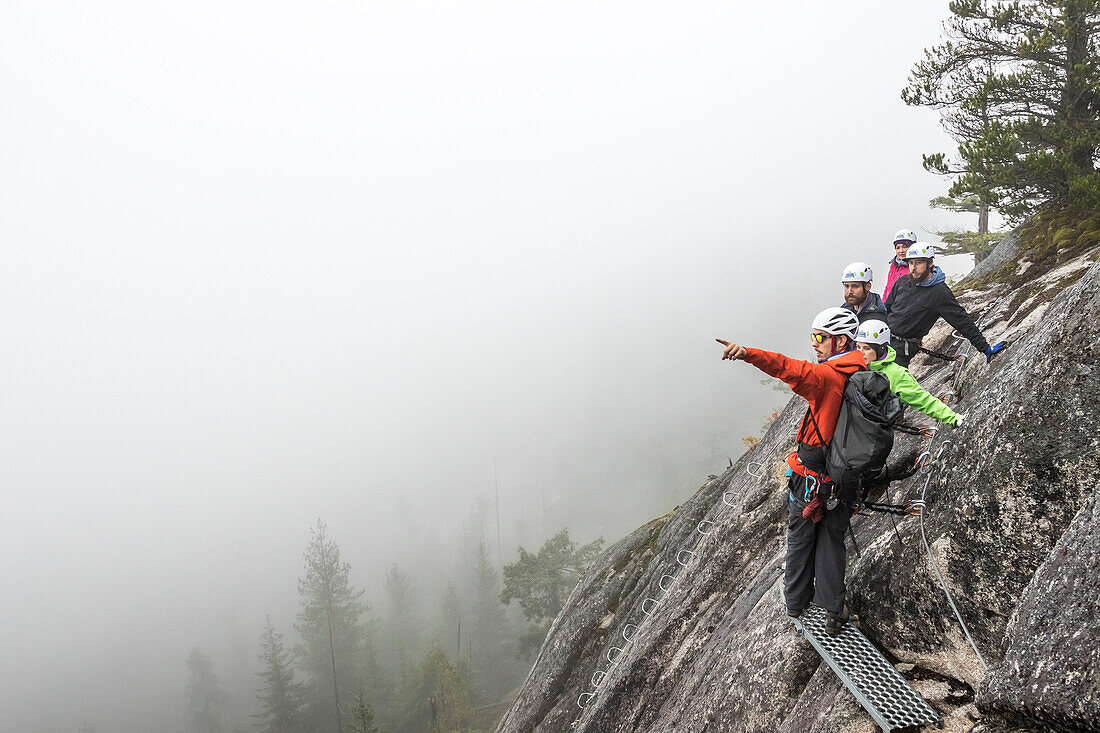 Ein Führer zeigt in den Nebel, um etwas zu einer Gruppe zu zeigen, die er auf einem Klettersteig in Squamish, British Columbia, führt.
