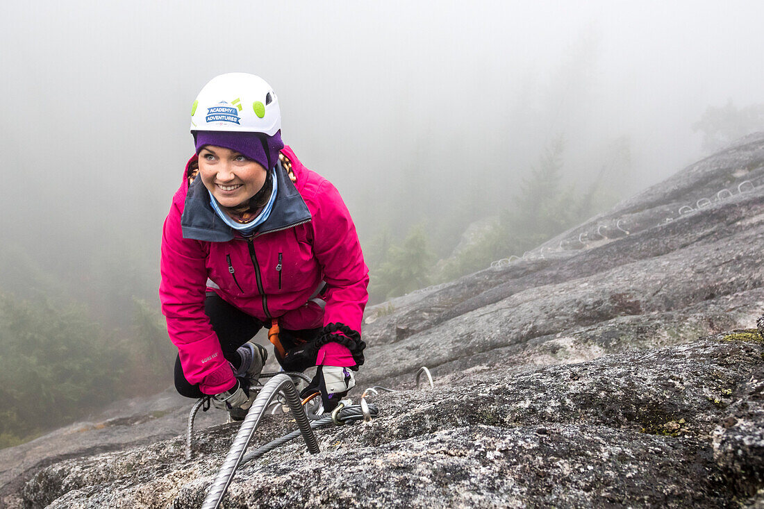 A women reaches for the metal rung while climbing the Via Ferrata in Squamish, British Columbia.