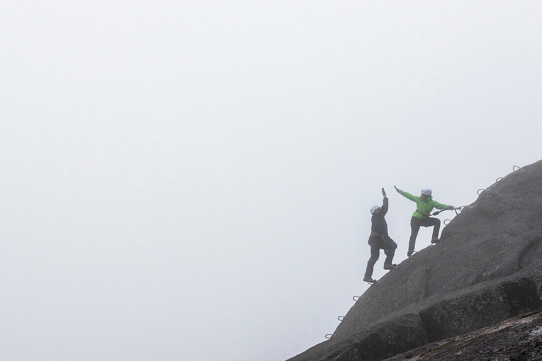 A man and a women slap a hi-five while doing the Via Ferrata on a rainy fall day in Squamish, British Columbia.