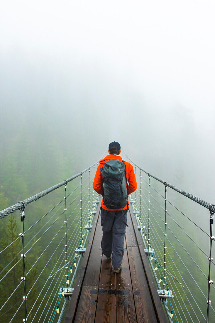 A man walks across a suspension bridge on a rainy fall day in Squamish, British Columbia.