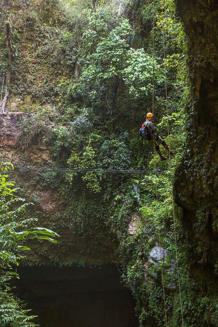 Eine Frau rappelt in eine tiefe Höhle in einem üppigen Wald in Puerto Rico