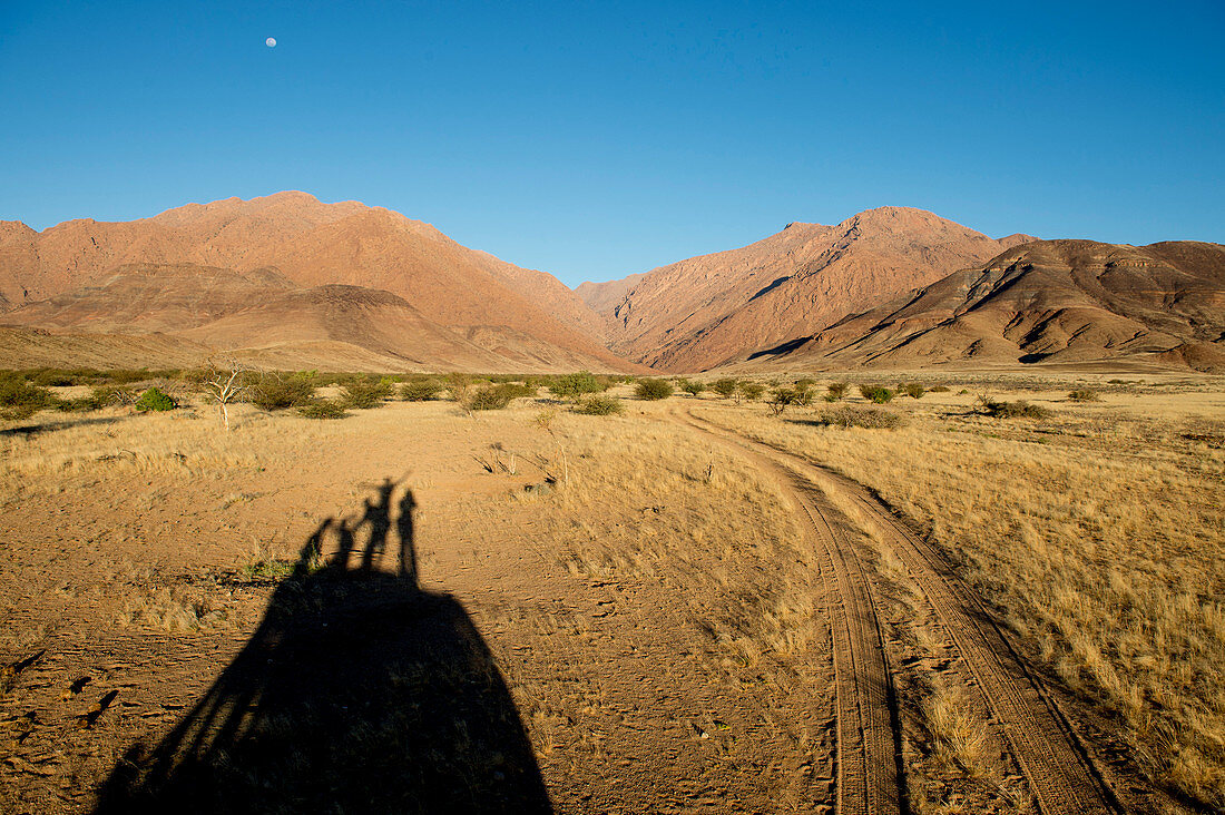 Photograph with shadow of four people on hill and scenery with hills, Brandberg mountain, Damaraland, Namibia