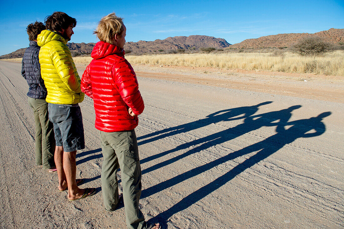 Three men in jackets casting long shadows on dirt road, Erongo region, Namibia