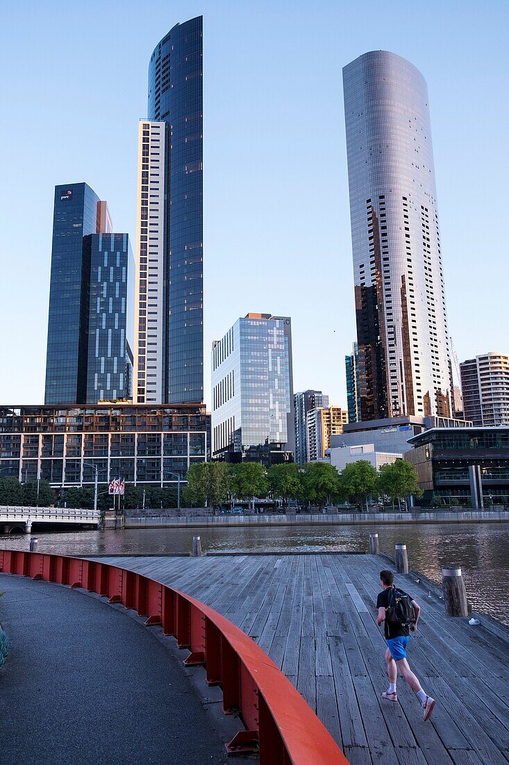 Mann joggt auf Enterprise Wharf mit Blick auf die Skyline von Southbank, Melbourne.