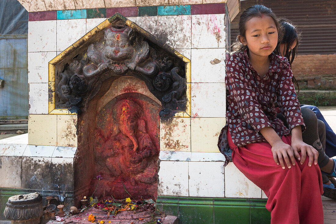 Bhaktapur, Kathmandu, Bagmati area, Nepal Little girl sitting beside the statue of Ganesh
