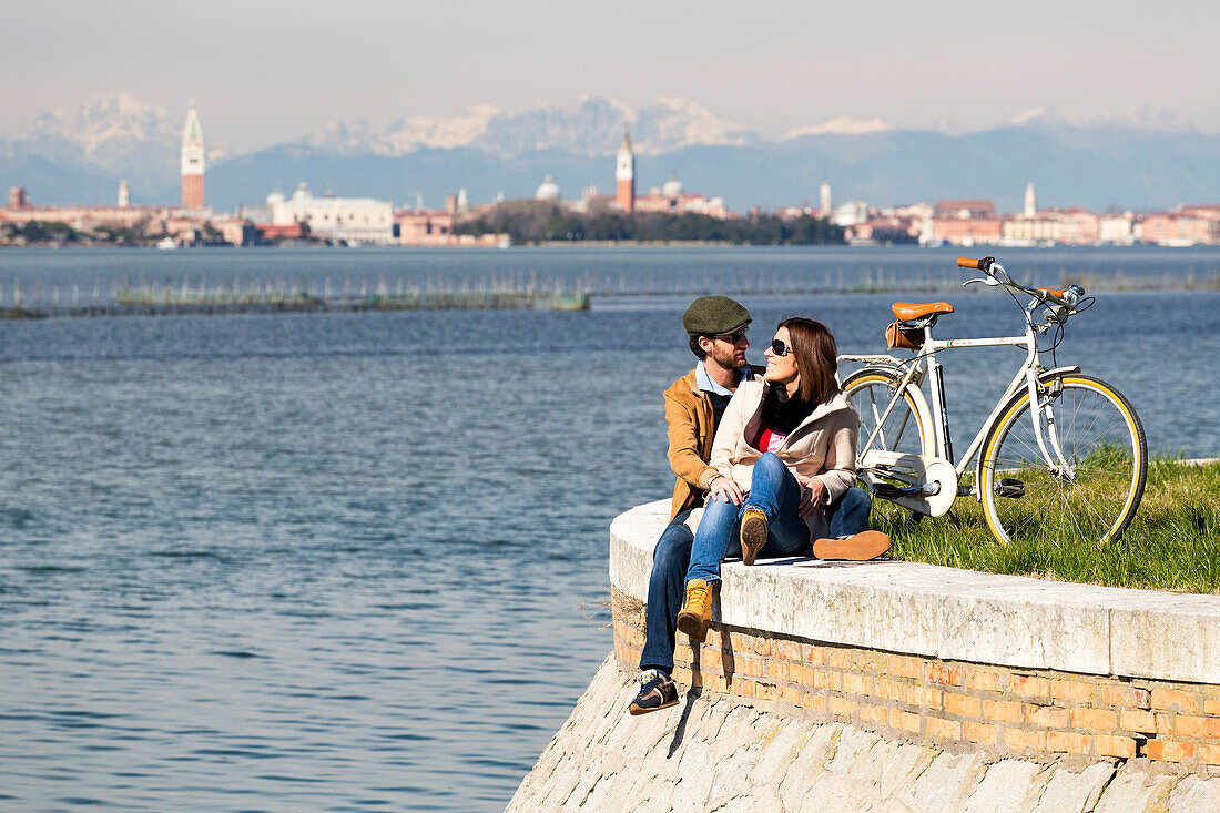 Ein paar entspannende am Ufer in Lido, im Hintergrund Venedig und die Dolomiten, Venedig, Venetien, Italien