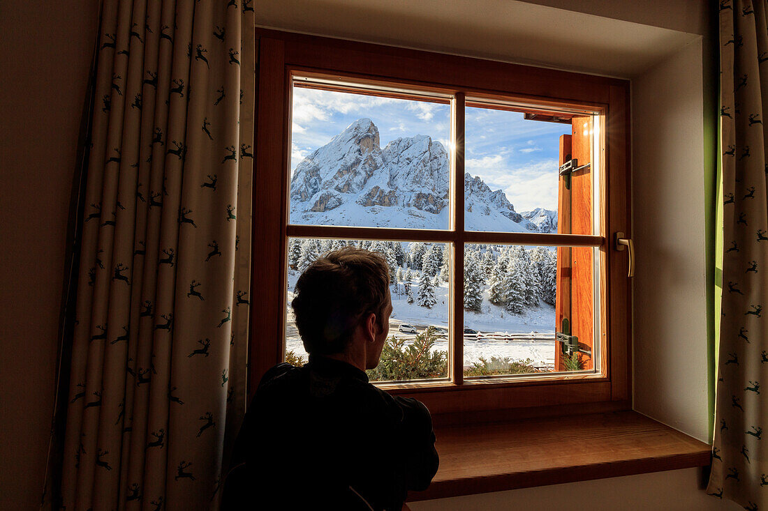 A man admires Sass De Putia surrounded by snow from the glass of a window Passo Delle Erbe Funes Valley South Tyrol Italy Europe
