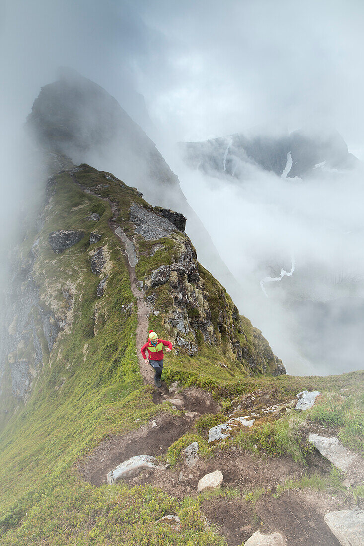 Hiker runs on the steep path on the peak of the Reinebringen mountain under the mist Moskenes Lofoten Islands Norway Europe