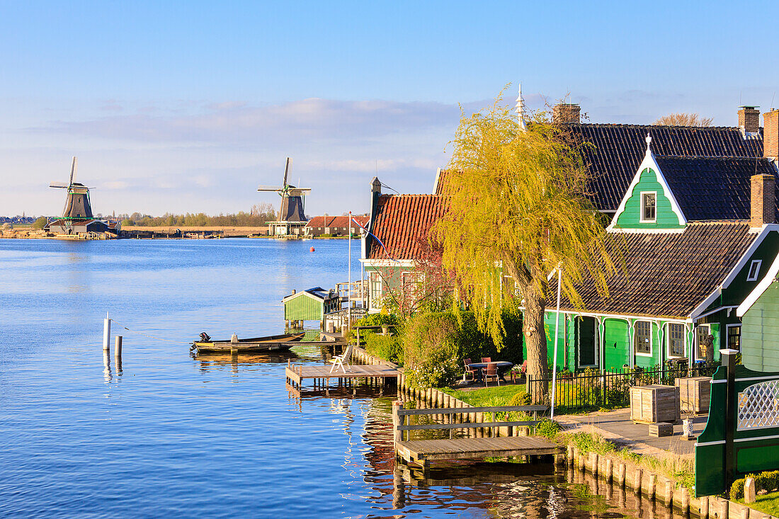 Holzhäuser und Windmühle spiegeln sich im blauen Wasser des Flusses Zaan Zaanse Schans Nordholland Niederlande Europa