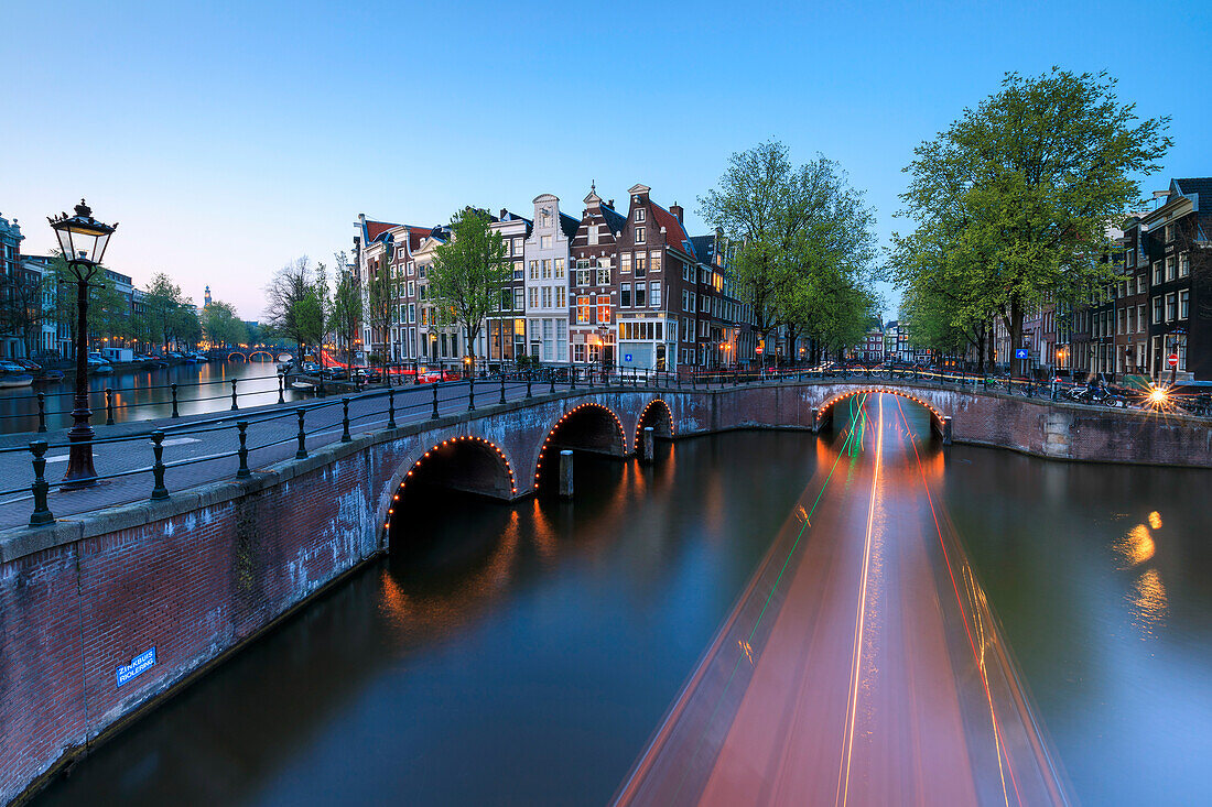 Dusk lights on the typical buildings and bridges reflected in a typical canal Amsterdam Holland The Netherlands Europe