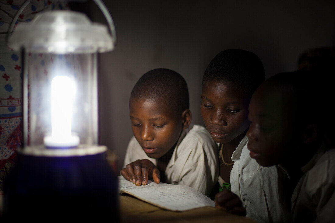 Eine Gruppe von Jungen liest ihre Hausaufgaben im Schein einer Sonnenlaterne, Tansania, Ostafrika, Afrika
