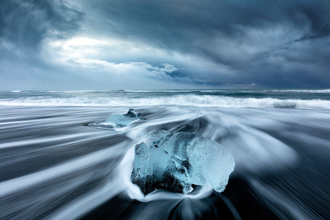 Gletschereis auf schwarzem Sandstrand mit den Wellen, die den Strand an einem stürmischen Wintertag, nahe Jokulsarlon, Süd-Island, polare Regionen abwaschen