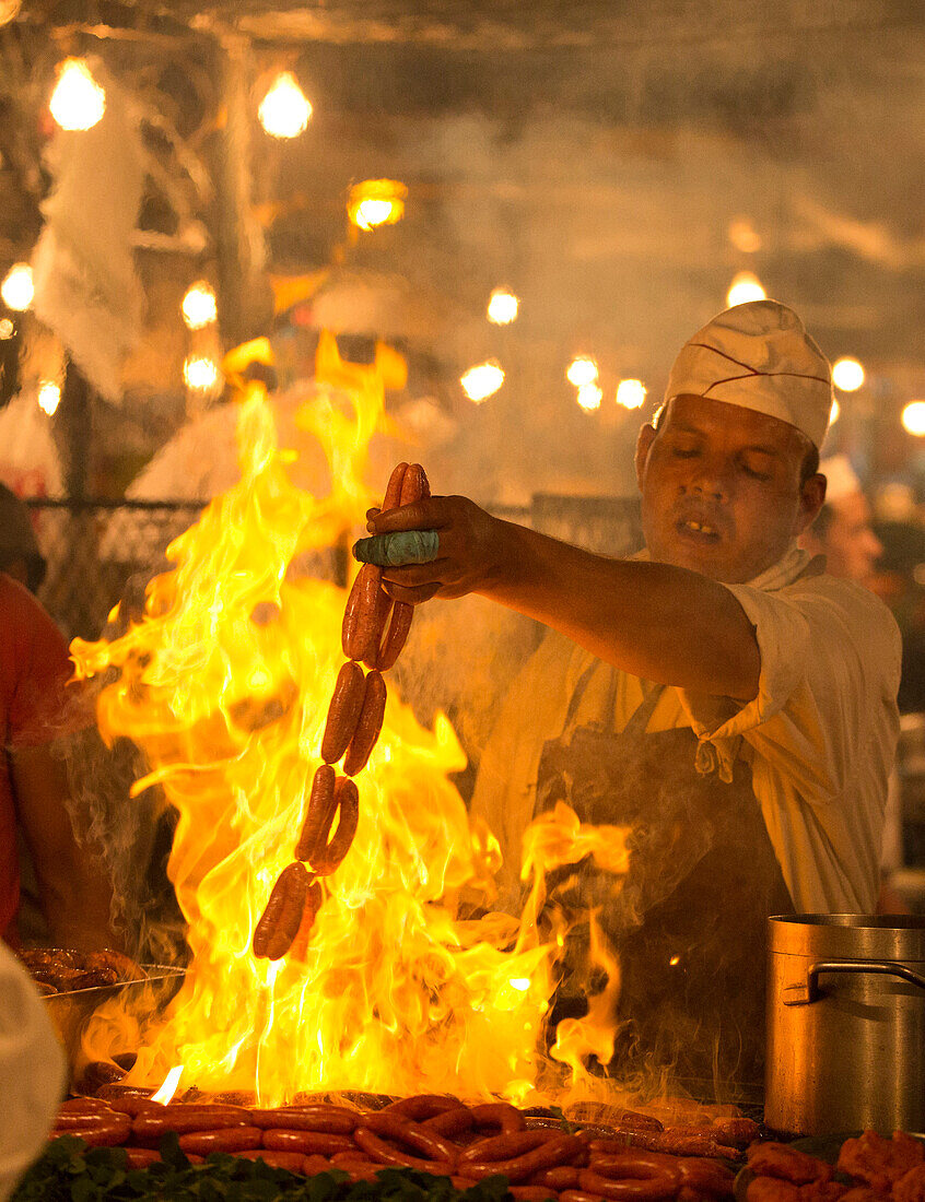 Lokaler Mann, der Würste auf offener Flamme an einem der Imbissstände im Djemaa EL Fna, Marrakesch, Marokko, Nordafrika, Afrika kocht