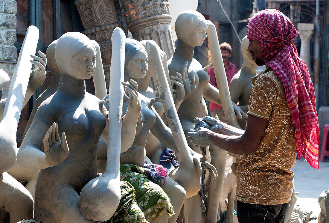 Sculptor adding hands to goddess Durga deities, made of Hooghly river clay over straw base in Kumartuli potters quarter, Kolkata ,Calcutta, West Bengal, India, Asia