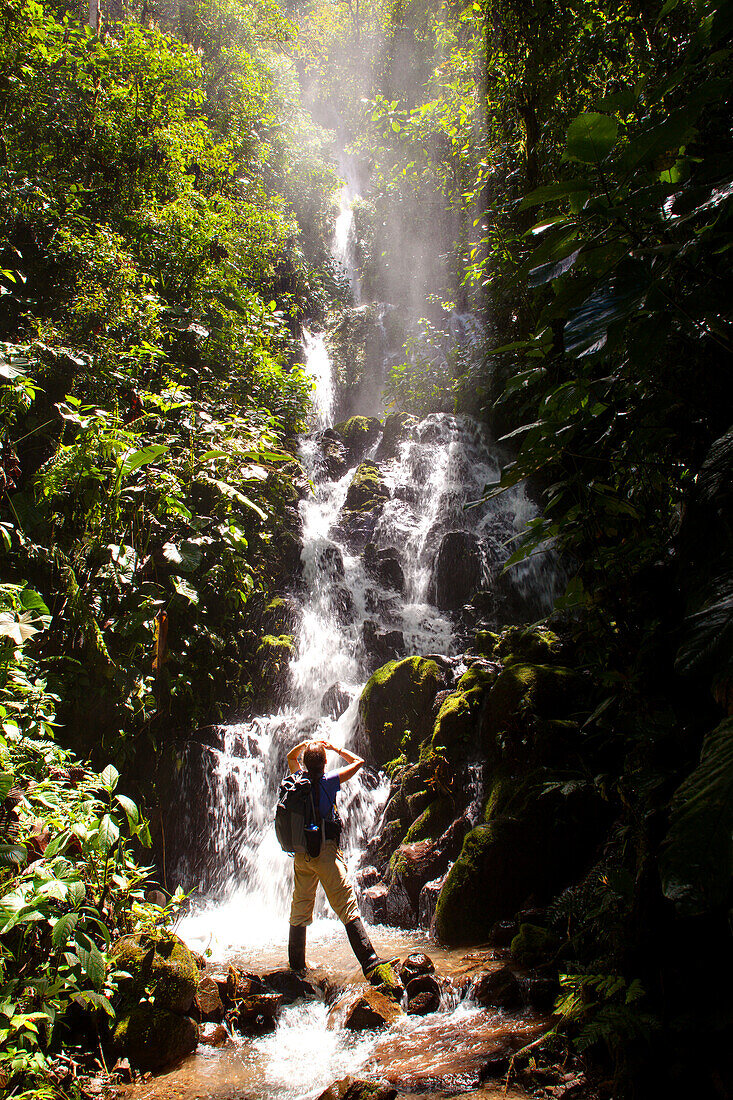 Female hiker below waterfall in the Santa Lucia Ecuadorian Cloud Forest Reserve, Ecuador