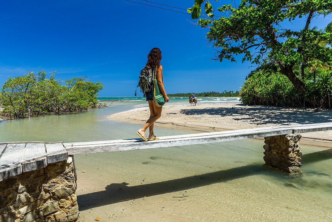 Woman walking over wooden bridge on tropical beach in South Bahia, Ilha de Boipeba, Brazil