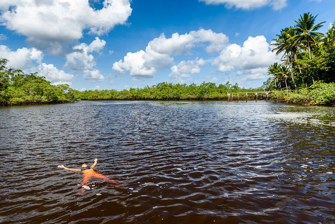 Woman floating on dark orange water in a tropical river, South Bahia, Peninsula de Marau, Brazil