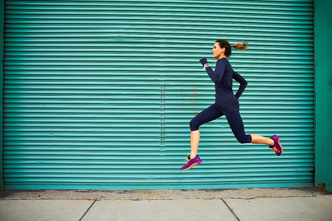 Female jogger running and jumping against green wall, Boston, Massachusetts, USA