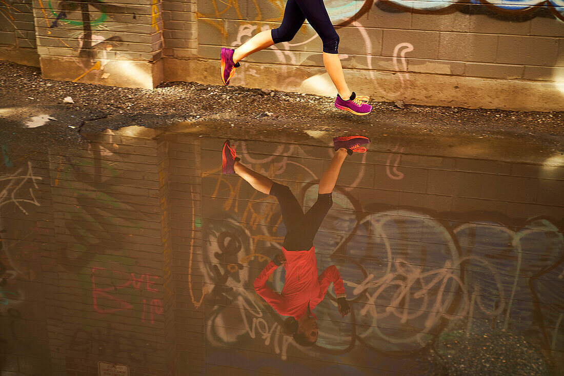 Woman running past puddle in graffiti lined alleyway in Boston, Massachusetts, USA