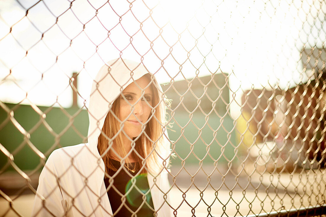 Portrait of woman touching chainlink fence and looking away, Boston, Massachusetts, USA