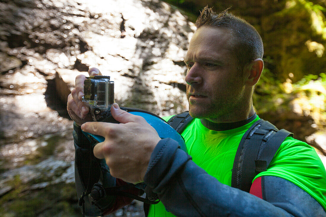 Photograph of man checking camera during canyoneering in Deneau Creek, Hope, British Columbia, Canada