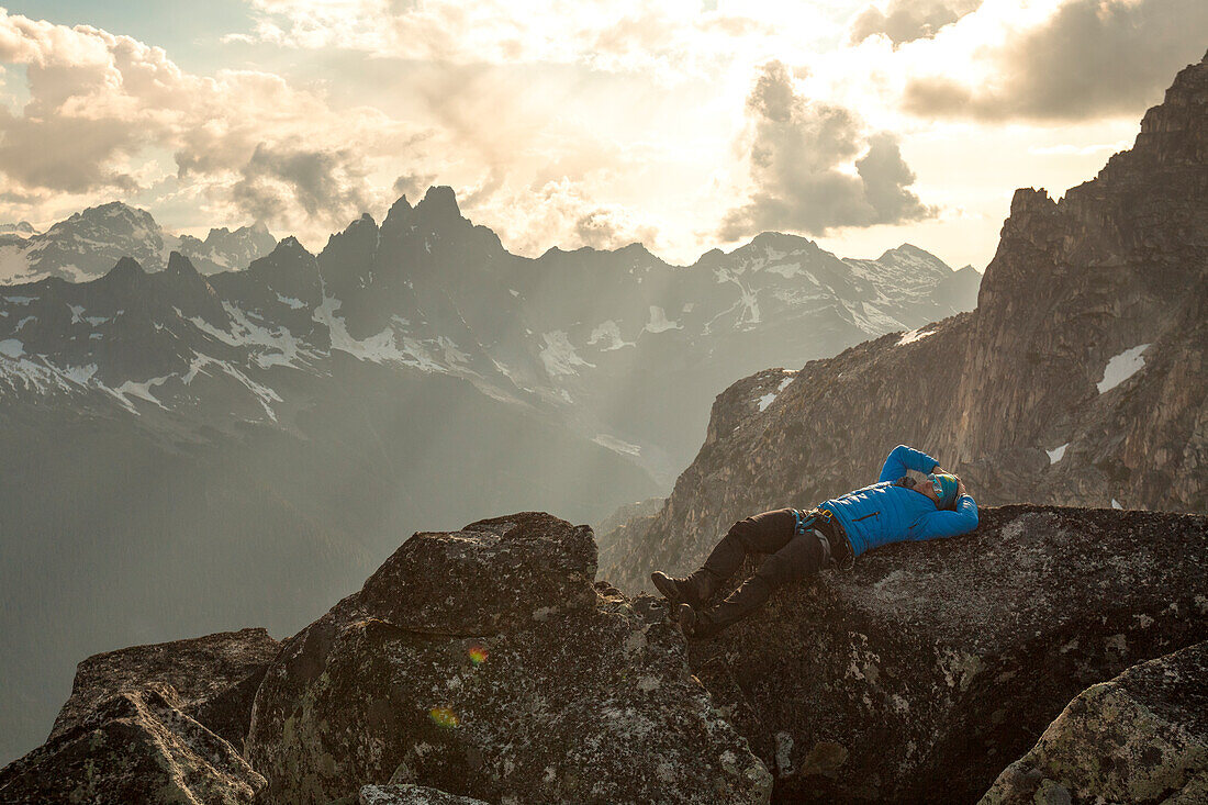 Photograph of mountain climber lying on back while resting at summit of mountain in North Cascade Mountain Range, Chilliwack, British Columbia, Canada