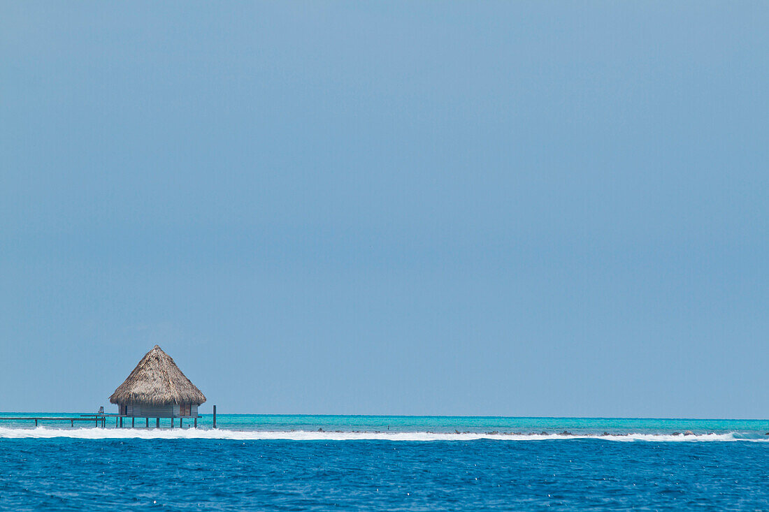 Thatched roof huts sit above the ocean off an island in the area of Glover's Reef, Belize.