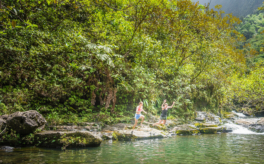 Two women jump into a swimming hole along the hike to Hanakapiai Falls on the Na Pali Coast of Kauai.