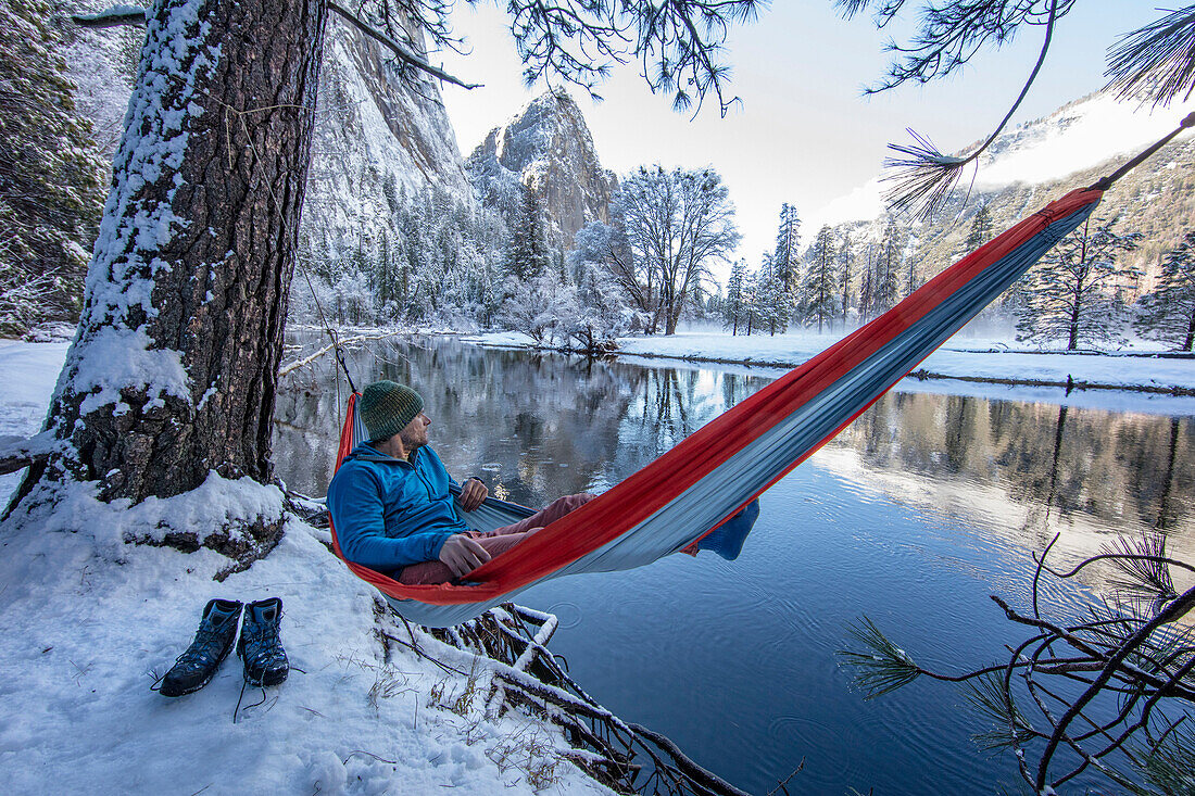 Fotografie des Mannes stillstehend in der Hängematte auf Seeufer während des Winters wandernd, hohe Sierra, Kalifornien, USA.