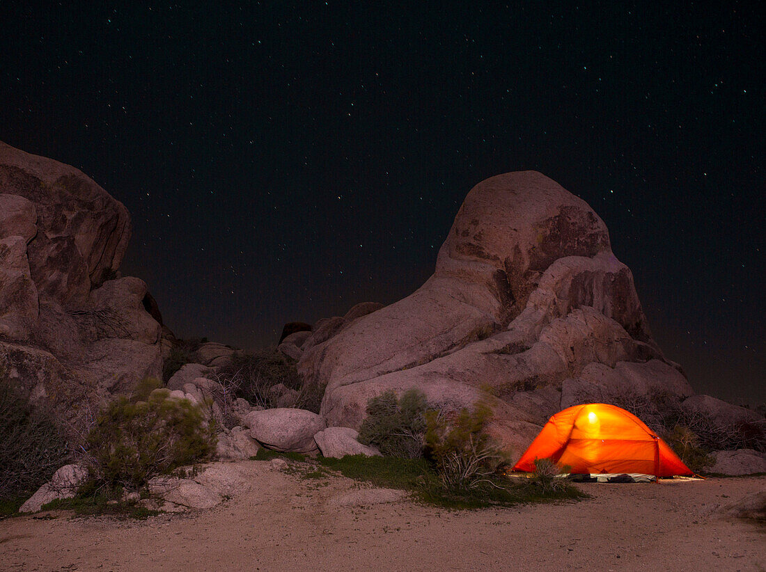 Tent lit up at night near rock formations in Indian Cove Campground in Joshua Tree National Park, California, USA