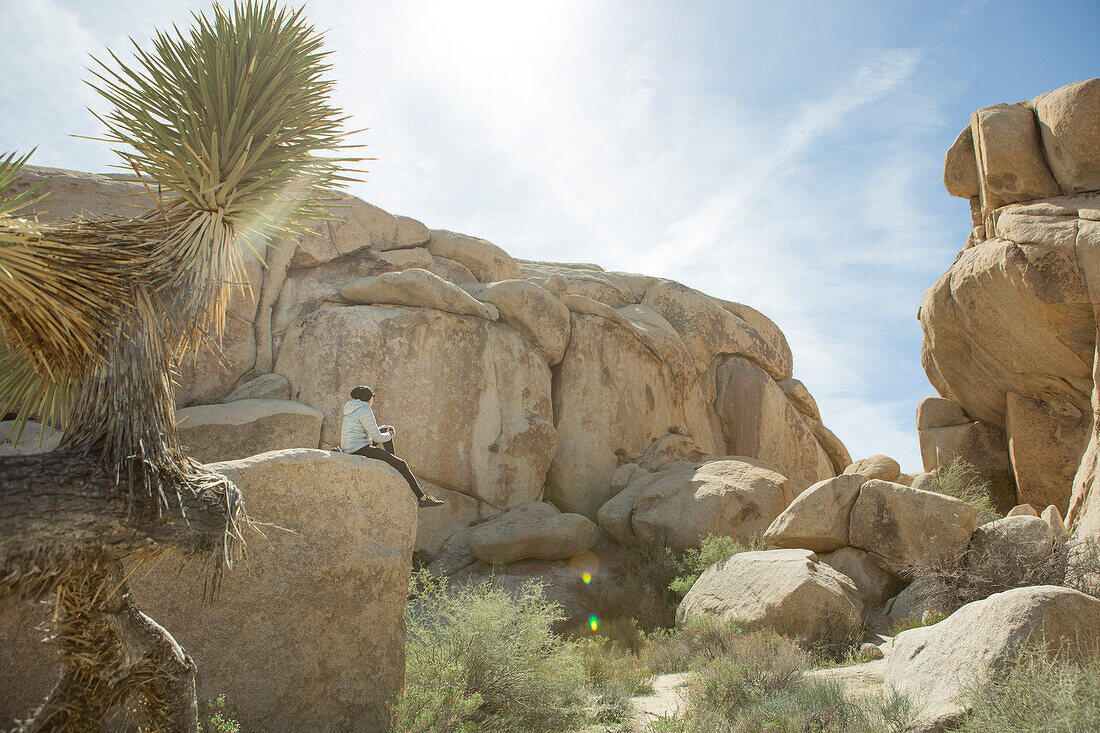 Photograph of woman sitting on large rock formation in Joshua Tree National Park, California, USA