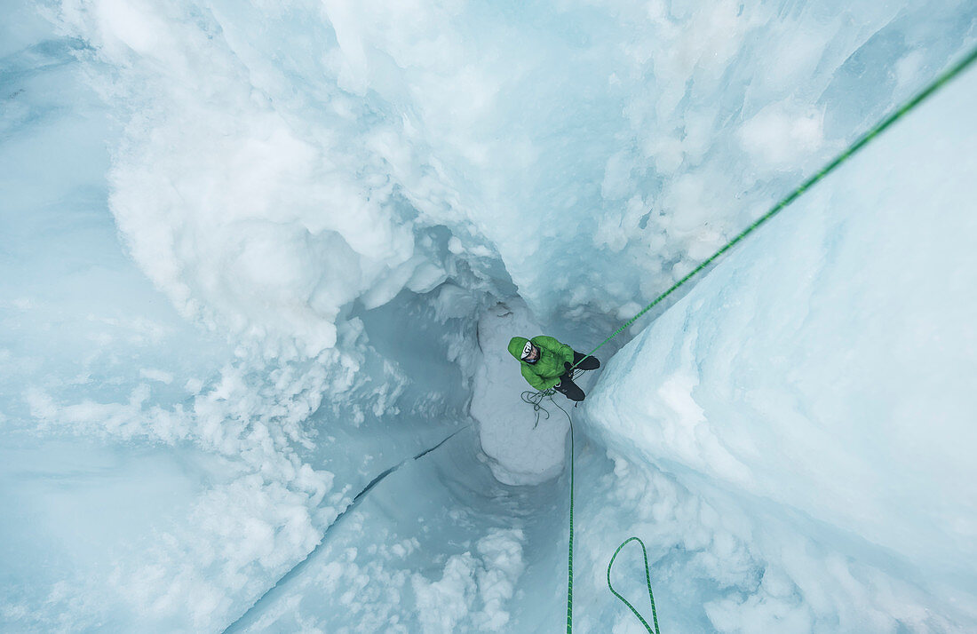 Photograph of adventurous man climbing out of glacial moulin, Coleman Glacier, Mount Baker, Washington State, USA