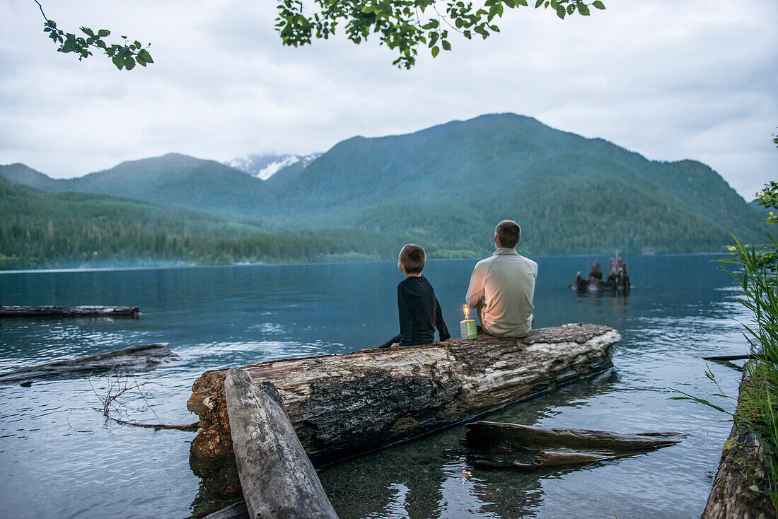 Ein Mann und sein Sohn sitzen nahe bei einem See bei Sonnenuntergang in Washington State.