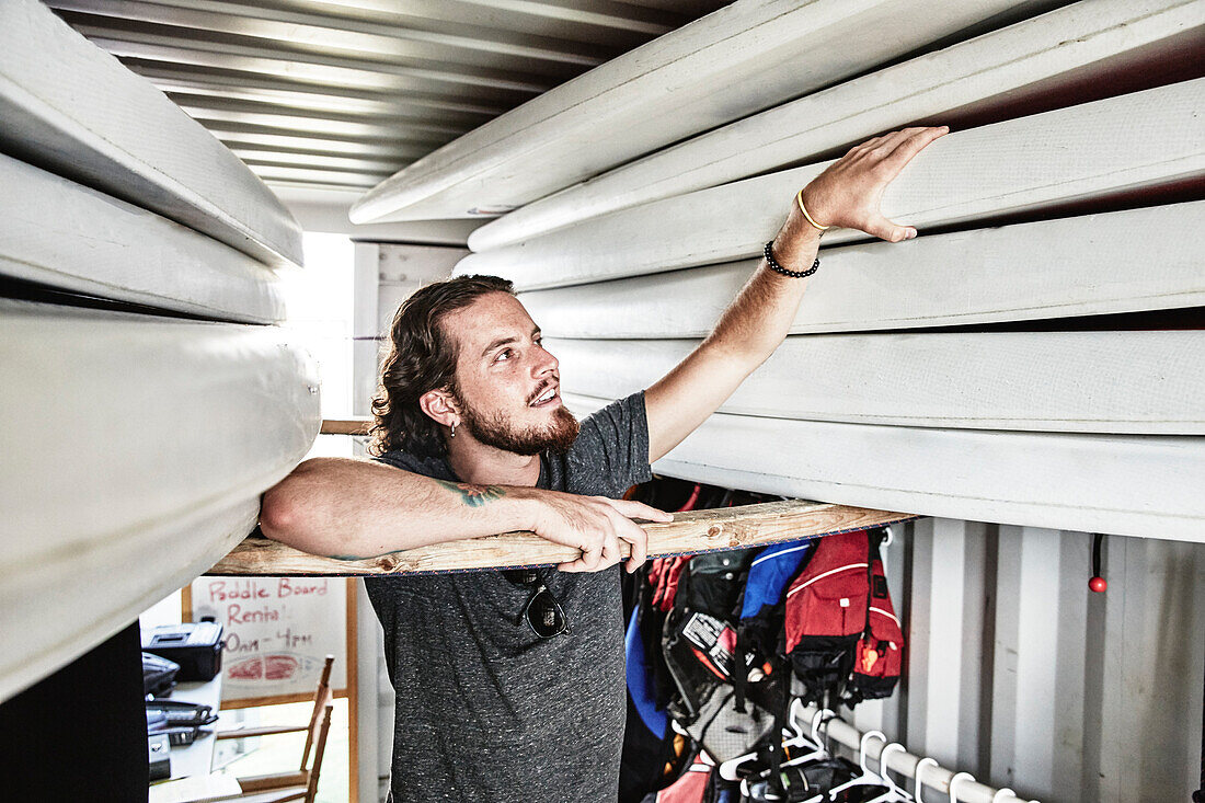 Young bearded man pulling paddleboard from container filled with swimming equipment, Portland, Maine, USA