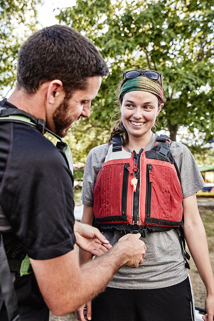 Man adjusting life jacket of female partner outdoors, Portland, Maine, USA