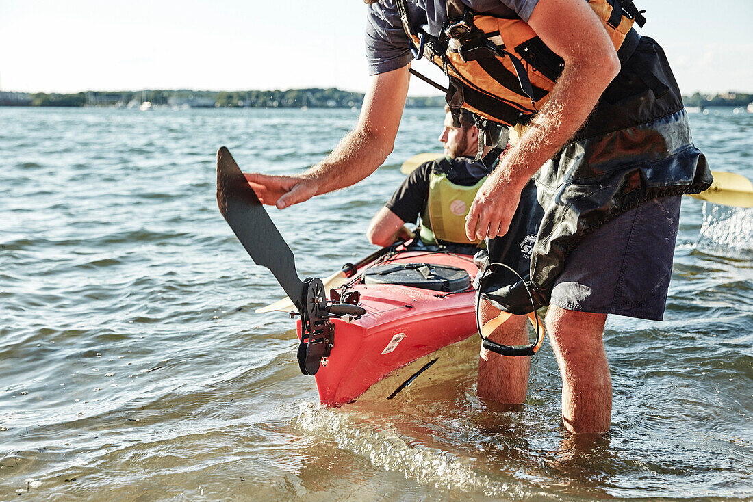 Photograph of kayak tour instructor lowering rudder on tandem sea kayak, Portland, Maine, USA