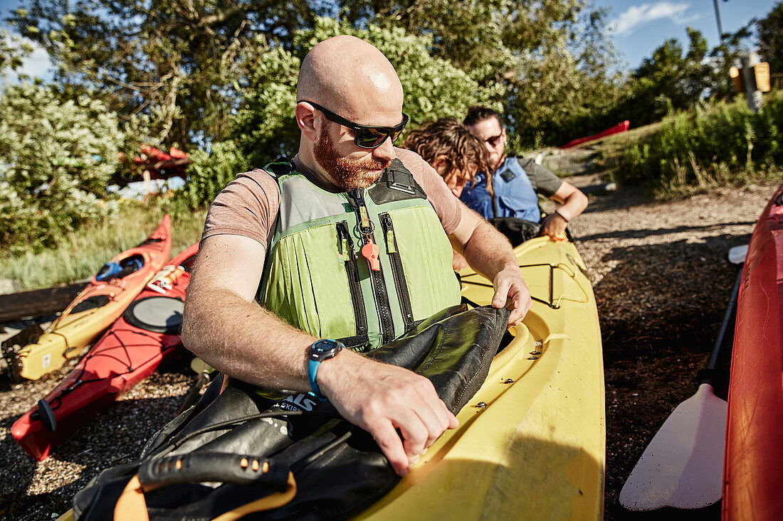 Photograph of kayak tour instructor helping two men attach their kayak skirts before sea kayaking, Portland, Maine, USA